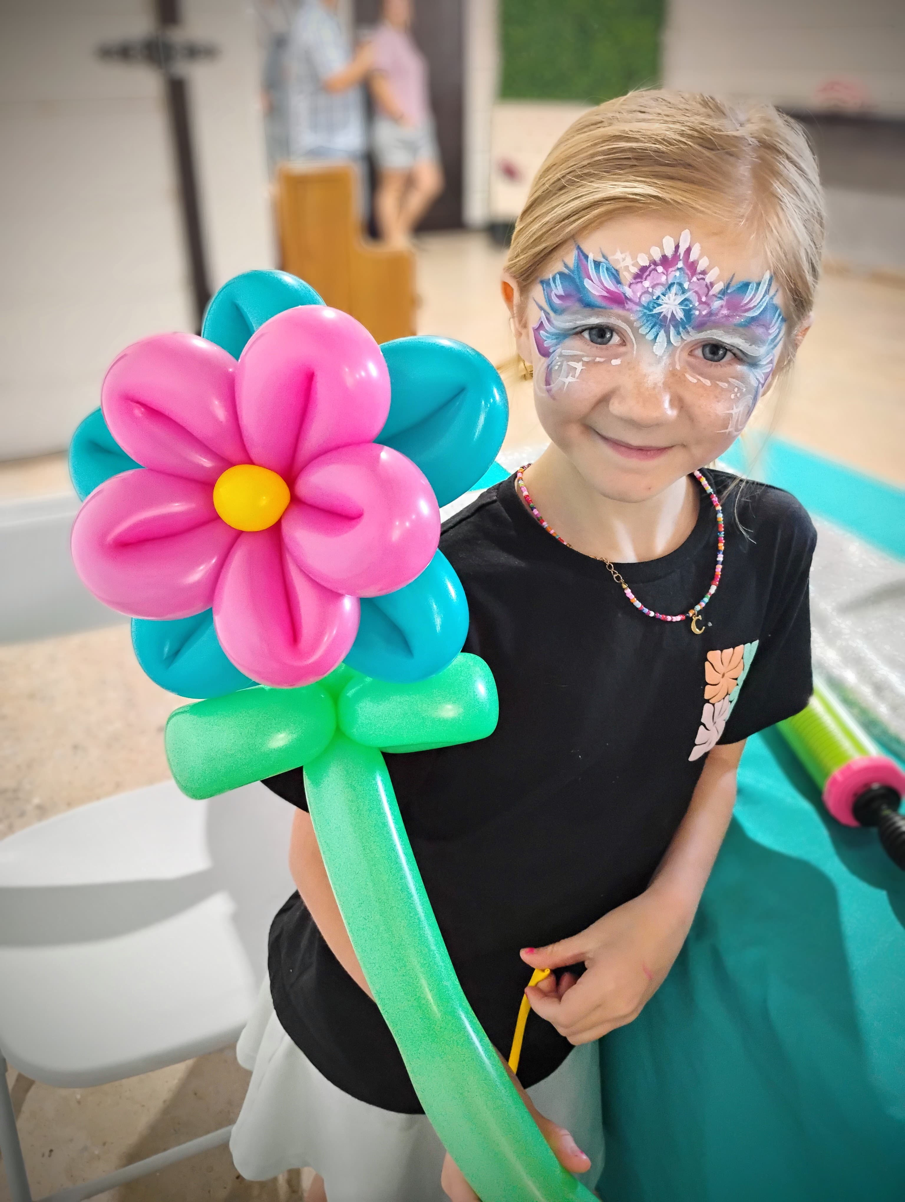 Girl with face paint holding a large balloon flower