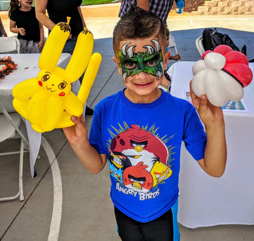 Boy with face paint holding Pikachu and Poké Ball balloons