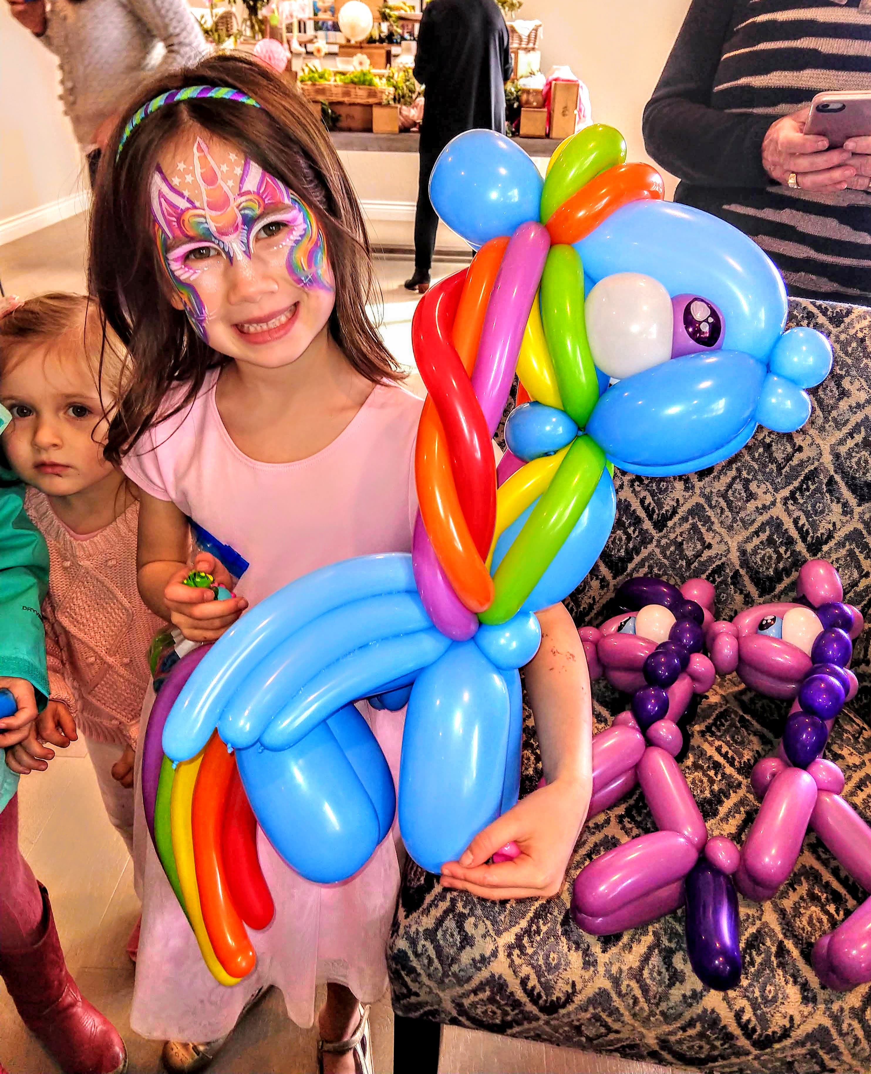 Girl with unicorn face paint and rainbow balloon pony