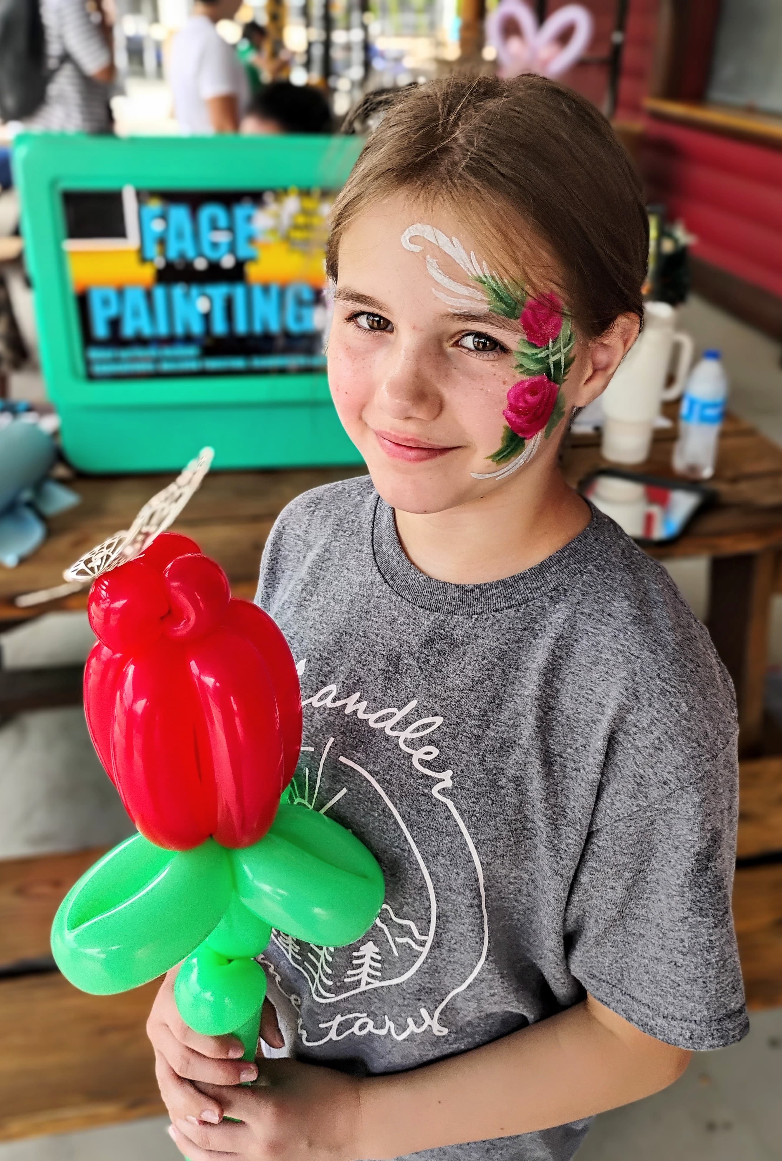 Girl with rose face paint holding a balloon rose
